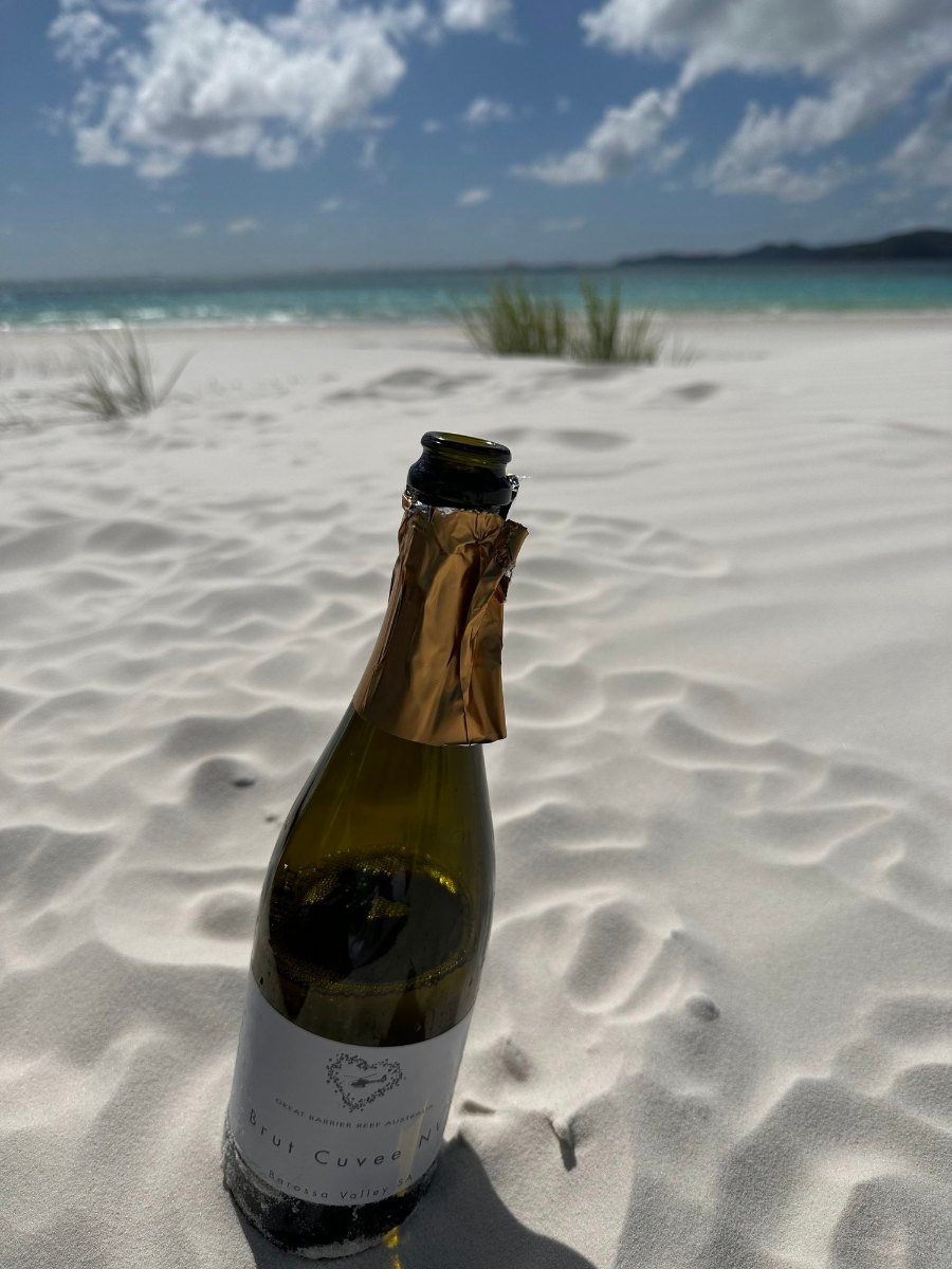 A bottle of bubbly standing in the rippled white sand