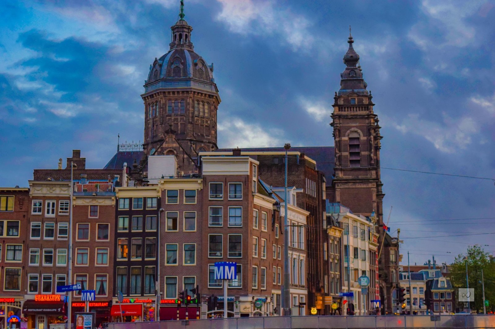 The dome and towers of the Basilica of St Nicholas, lit up above a row of old houses against a deep blue evening sky