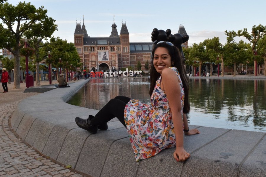 Meenu laughing on the edge of the pond at Museumplein, with the Rijksmuseum and the I amsterdam letters behind