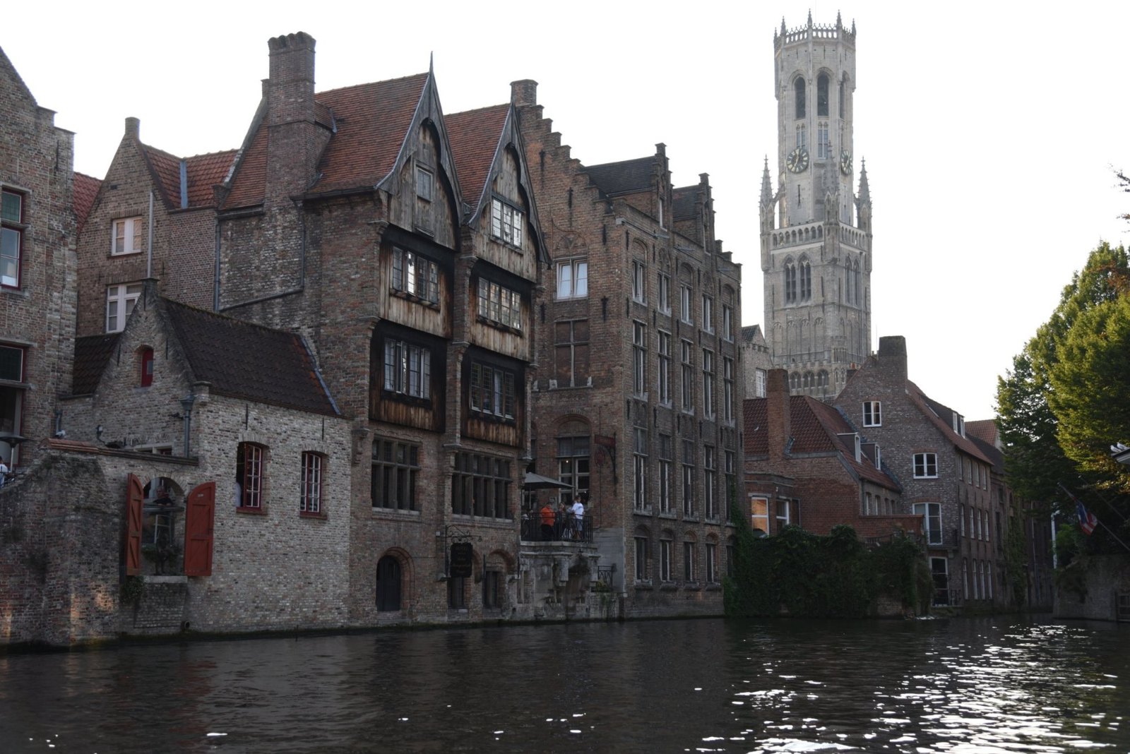 Old brick houses and gables rising from the canal at the Rozenhoedkaai in Bruges, with the Belfry behind