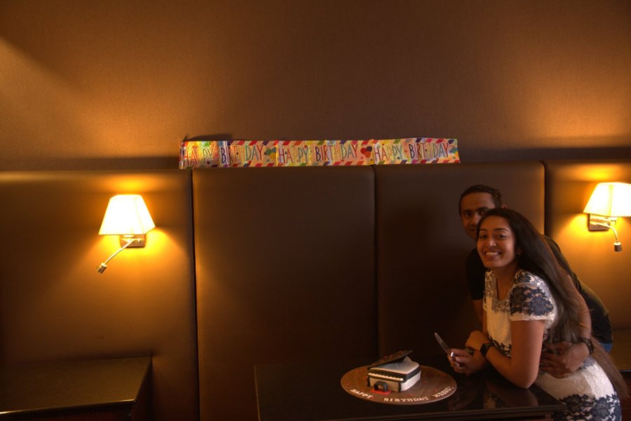 Meenu and Praddy smiling beside her grand-piano birthday cake in our hotel room