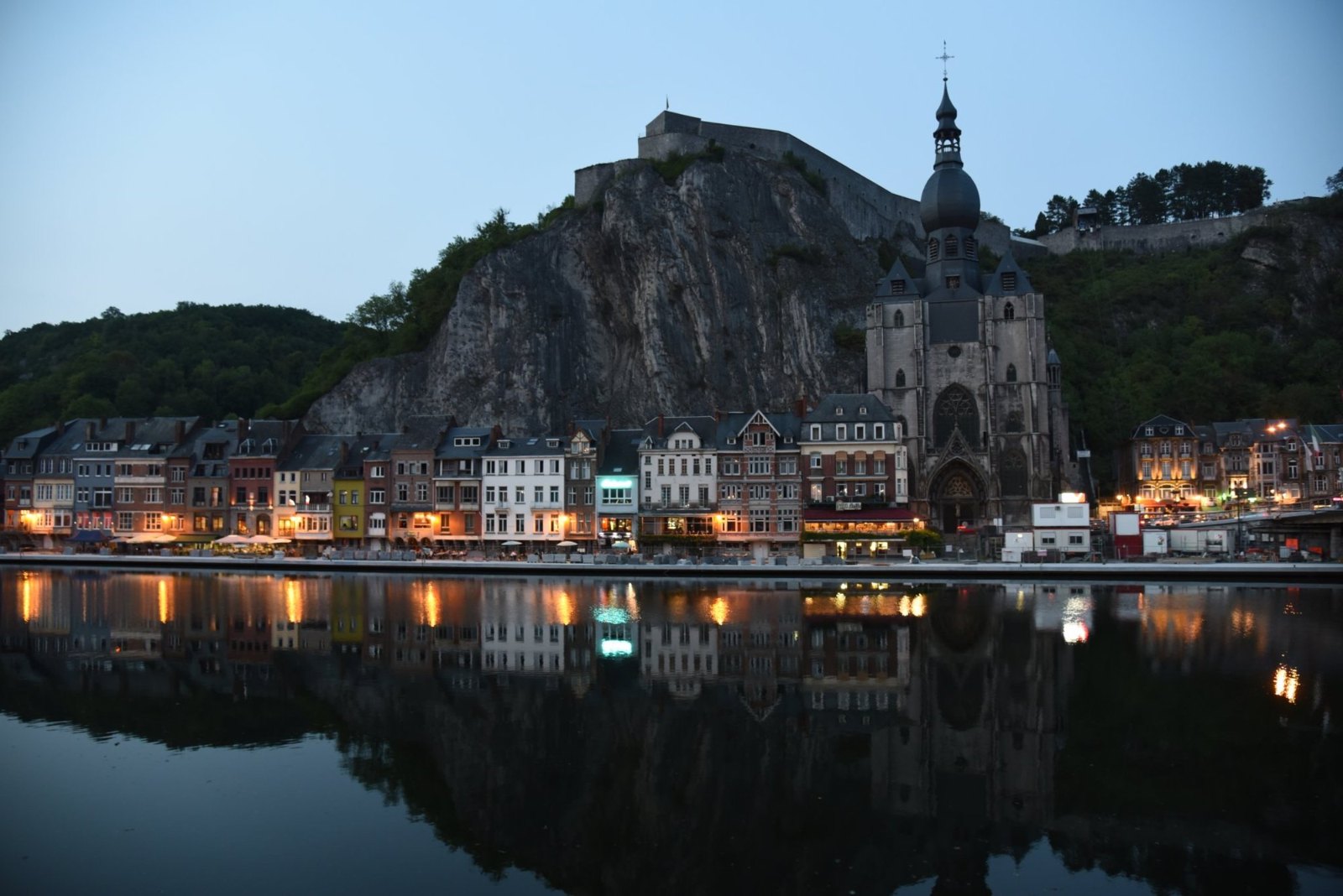 Dinant at dusk, its lit quay and onion-domed church tower mirrored in the Meuse below the citadel cliff