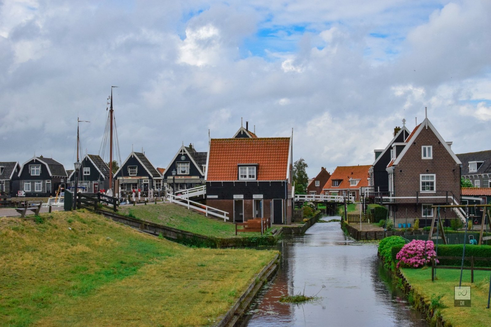 A narrow canal running between Marken's dark wooden houses and red roofs, with a boat's mast beyond