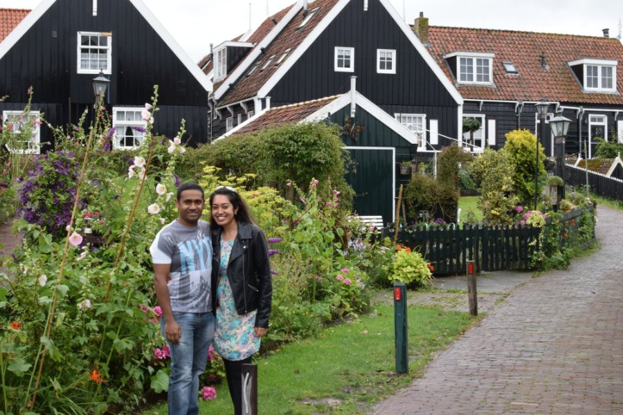 Praddy and Meenu in a garden of hollyhocks in front of Marken's black wooden houses