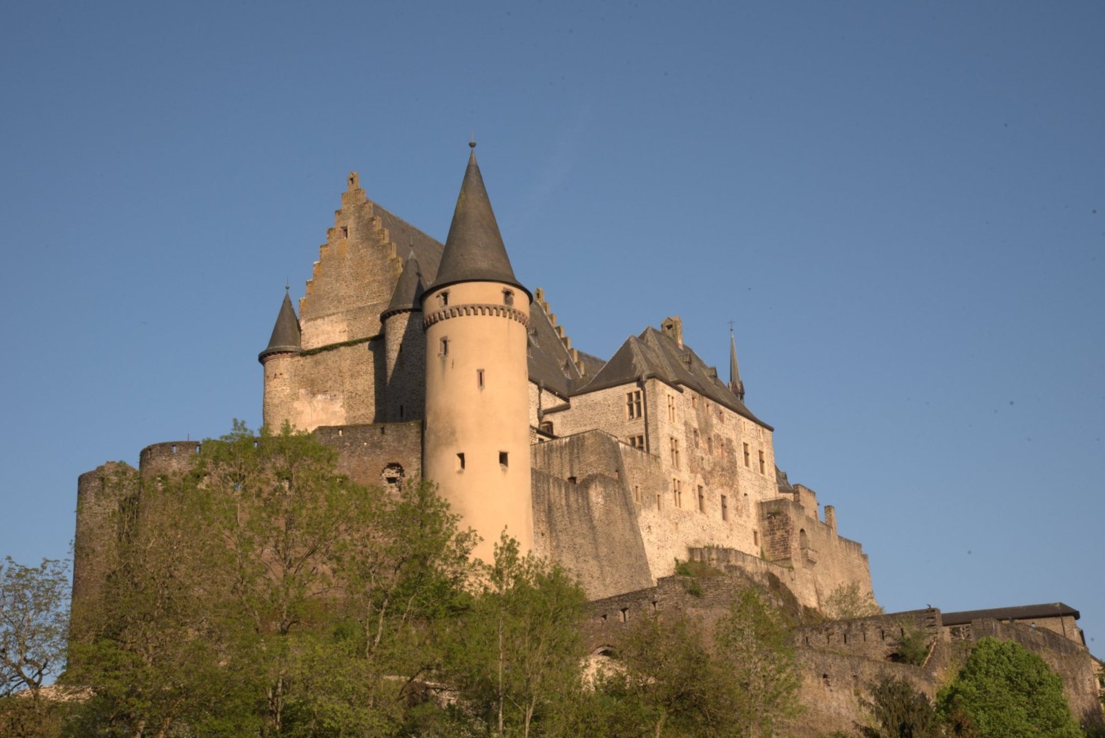 Vianden Castle's pale walls and pointed turrets on its hill, lit by the evening sun