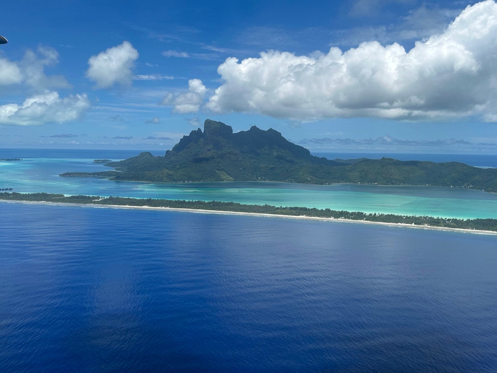 Bora Bora from the Air Tahiti plane, with Otemanu rising behind the lagoon and a long sandy reef island
