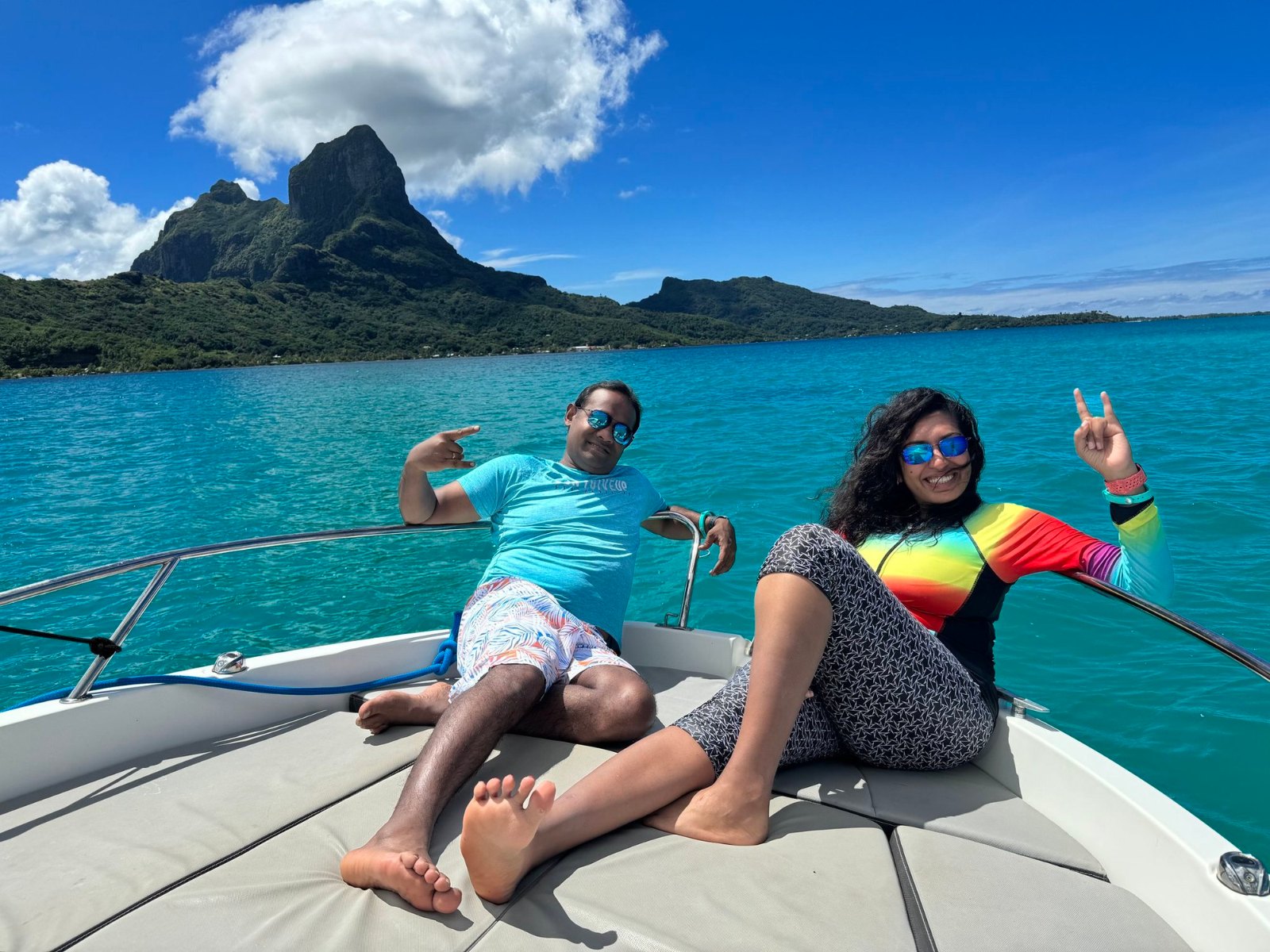 Meenu and Praddy stretched out on the bow of a boat on the turquoise lagoon, with Otemanu behind