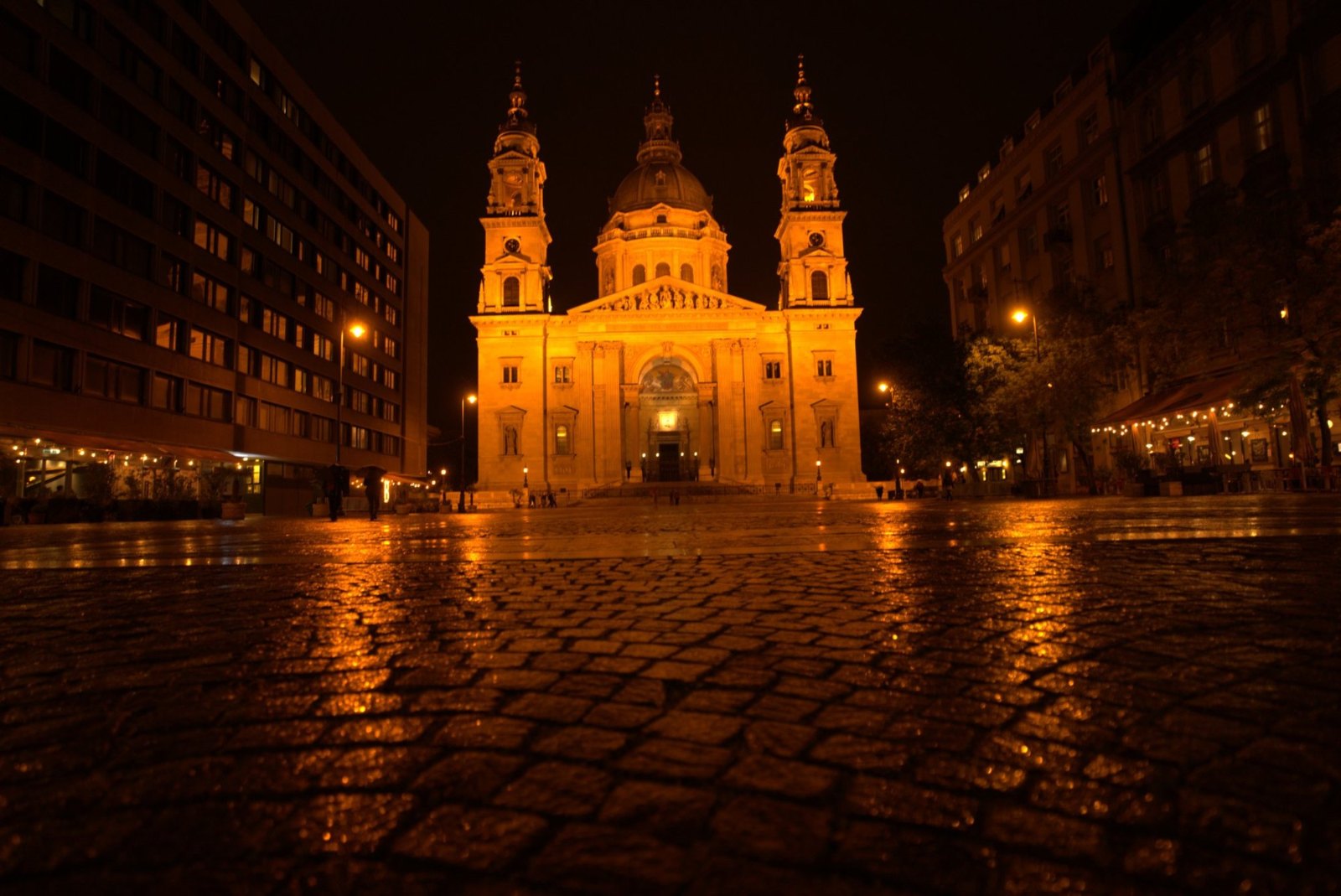 St Stephen's Basilica lit up at night, its two towers and dome reflected in the wet cobbles of the empty square
