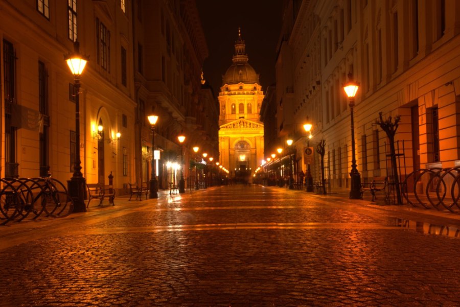 A wide pedestrian street at night, lined with lamps, leading to the Basilica's lit dome