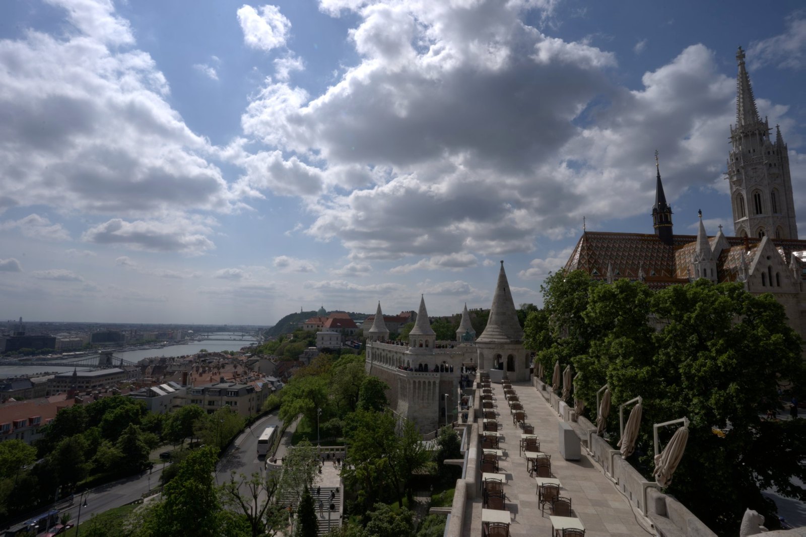 Fisherman's Bastion's white turrets and terraces under big clouds, with Matthias Church's spire above and the Danube below