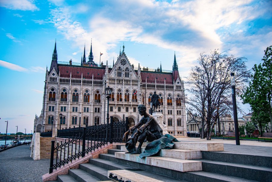 A bronze man sitting on the steps by the river, with the Parliament behind him in the early morning