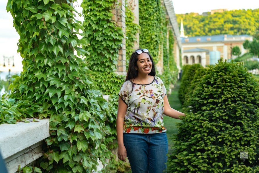 Meenu smiling among ivy-covered columns and clipped conical trees