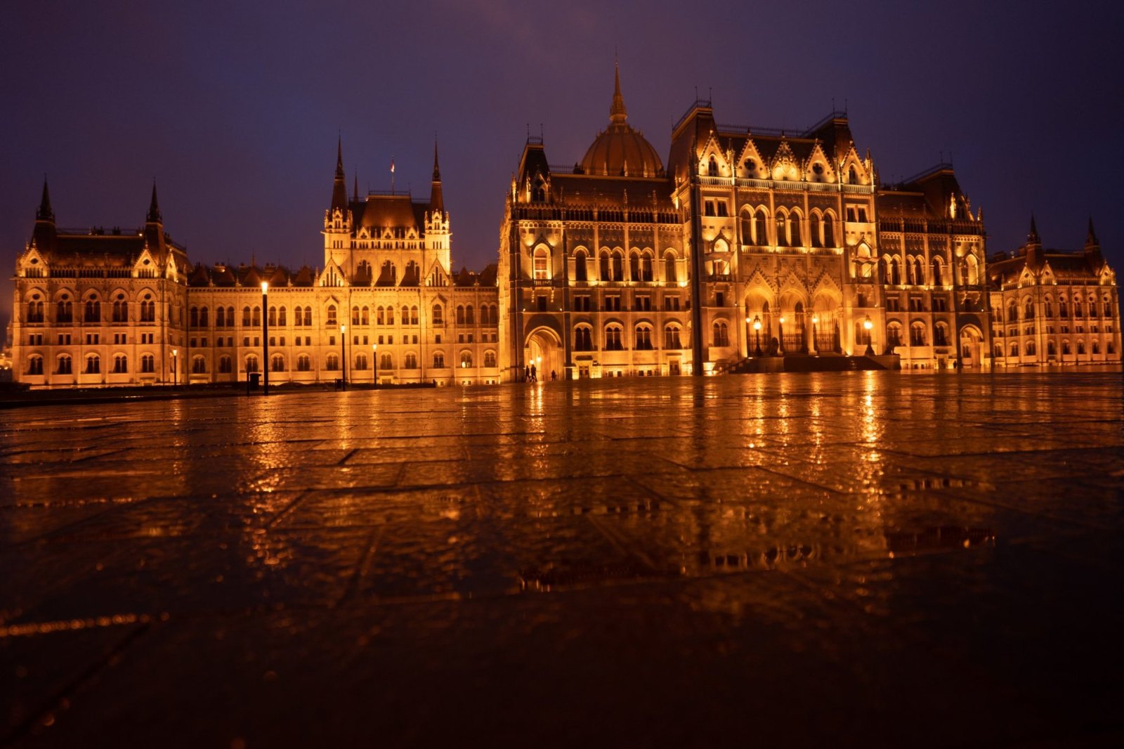 The Parliament's façade lit gold at night, reflected in the wet stone of the square