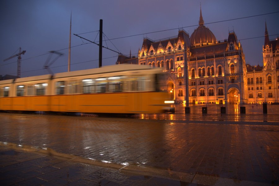 A yellow tram blurring past the lit Parliament under a purple dusk sky