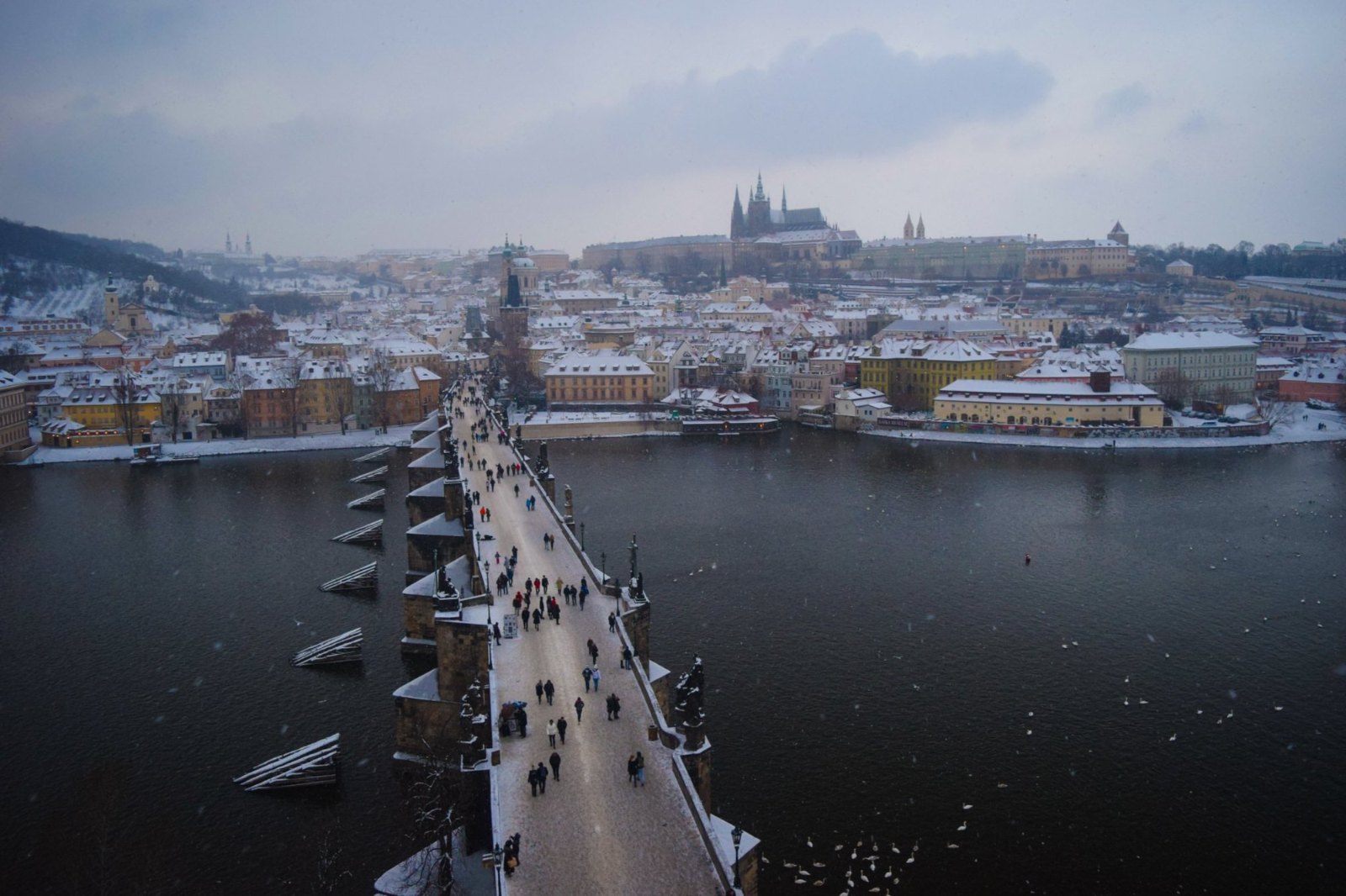 Charles Bridge under snow, seen from its Old Town tower, crossing the Vltava toward Prague Castle on the hill