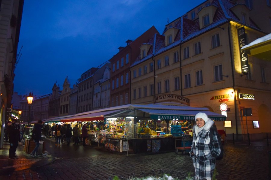 Meenu in a white knitted hat beside market stalls lit up at dusk under snowy roofs