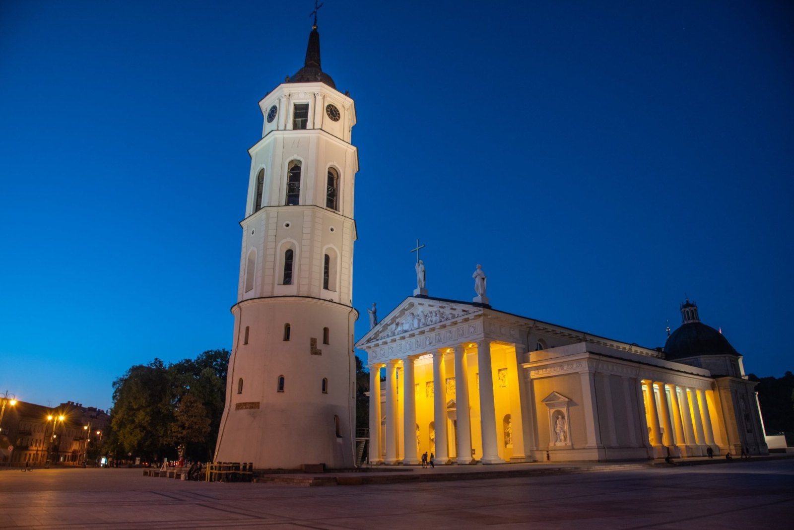 Vilnius Cathedral's white bell tower beside the cathedral's floodlit columns under a deep blue sky
