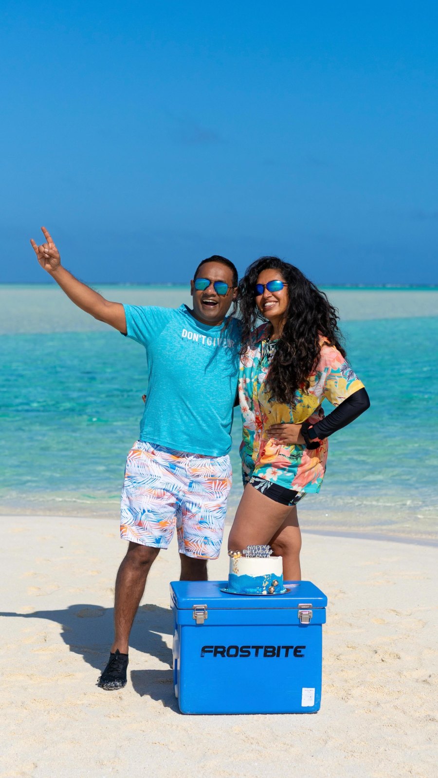Praddy and Meenu on white sand in the lagoon, with a blue cool box at their feet