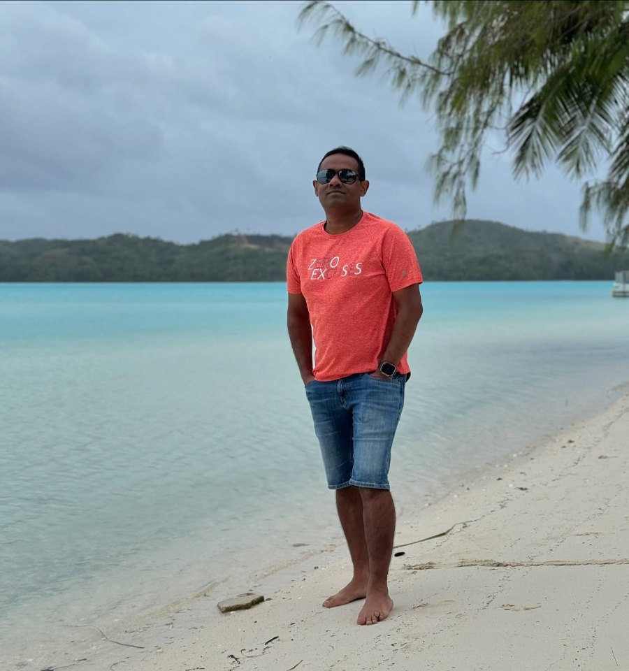Praddy on Ootu Beach, with the shallow lagoon and green hills behind him
