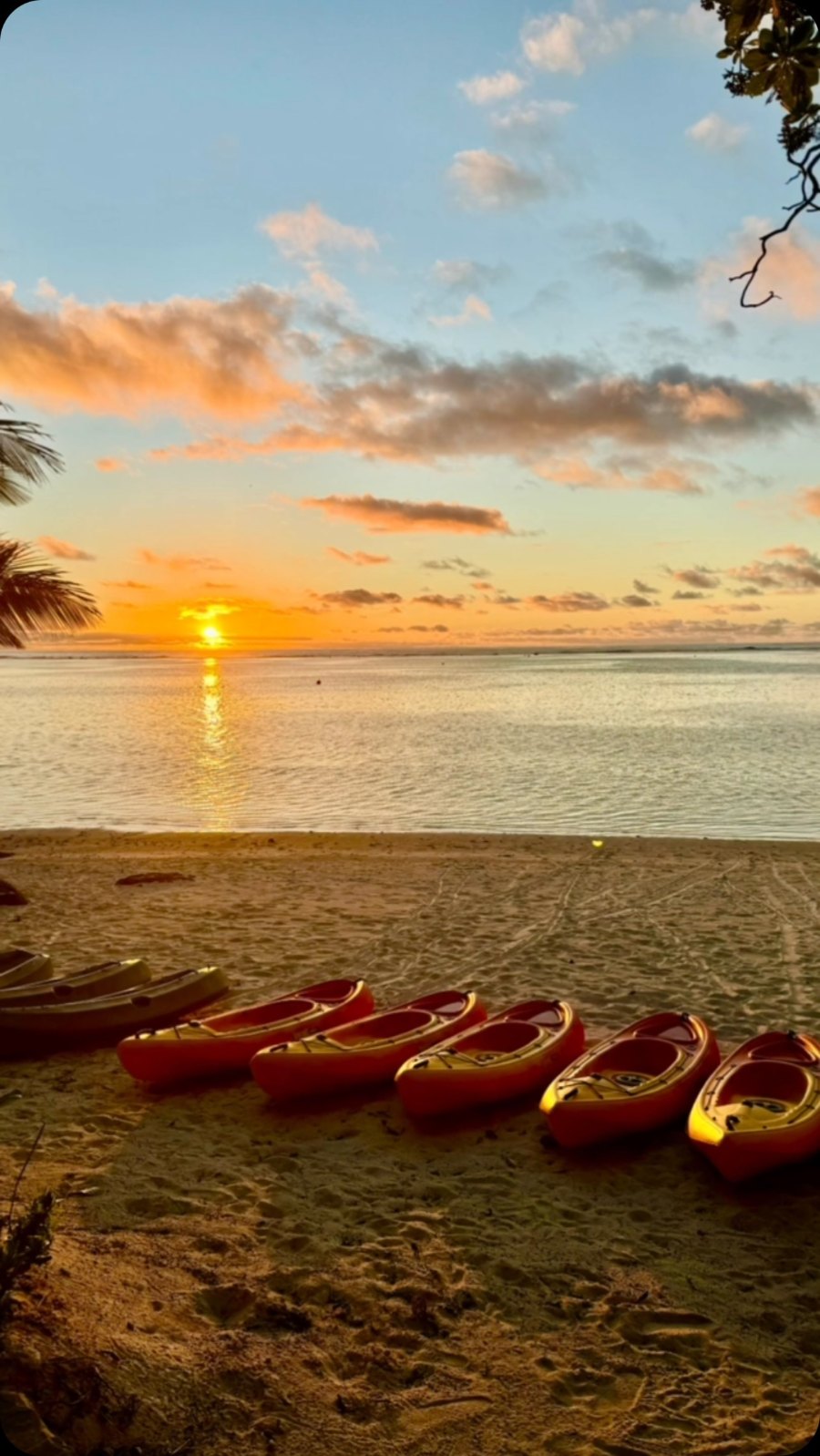 The sun going down over the water at Pacific Resort Aitutaki, with kayaks lined up on the sand