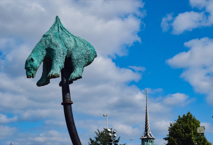 A green bronze polar bear impaled on a tall pole, against a blue sky