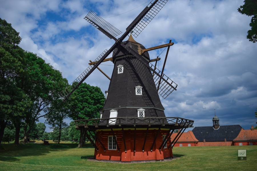 Kastellet's black windmill, with red barracks behind, under a cloudy sky