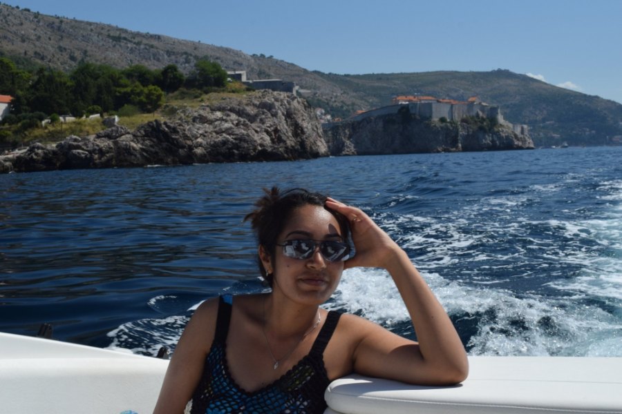 Meenu at the back of the speedboat, with the white wake and the cliffs behind her