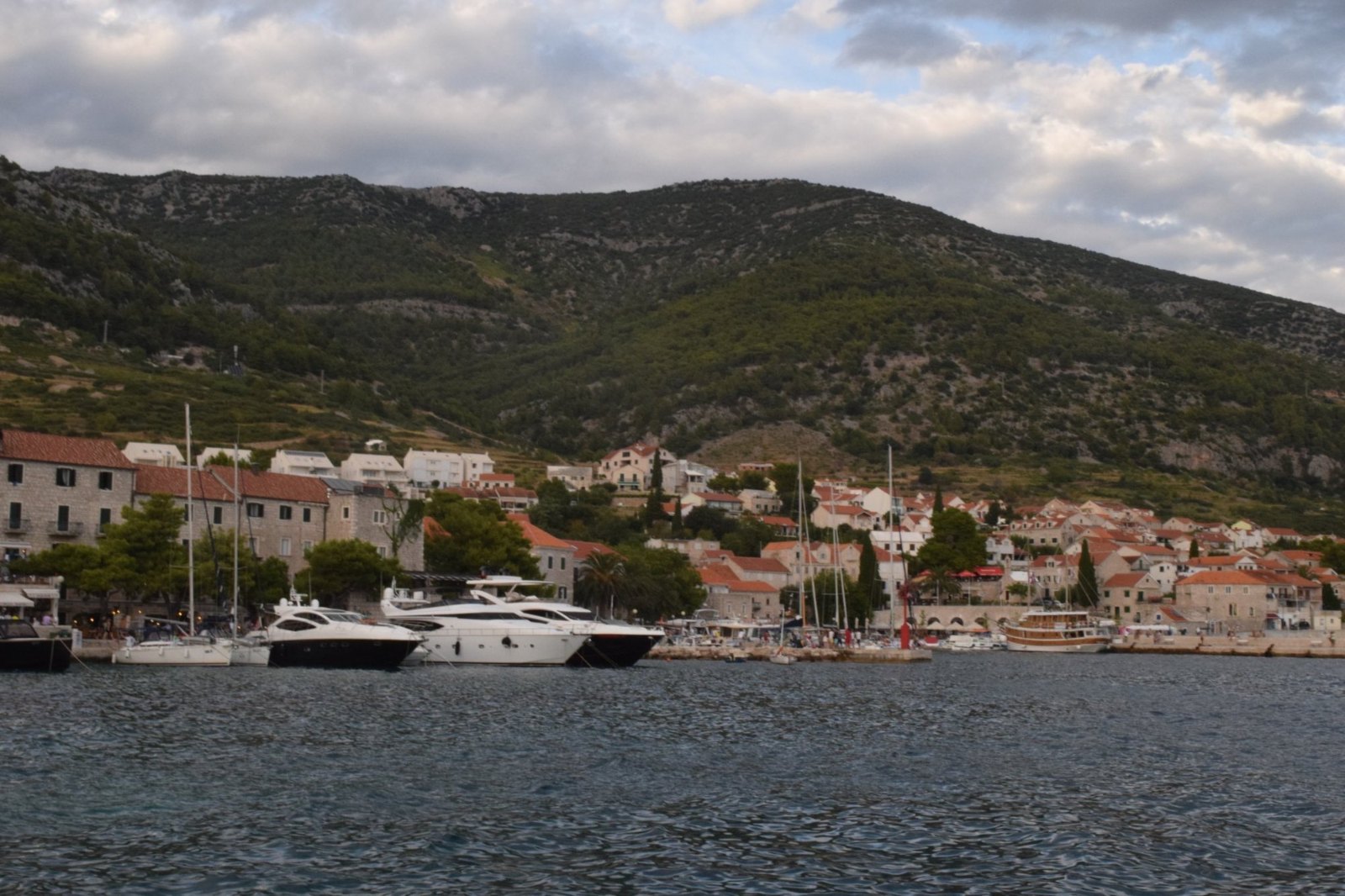 Bol's old stone houses and moored motor yachts along the harbour, below the long green slope behind the town