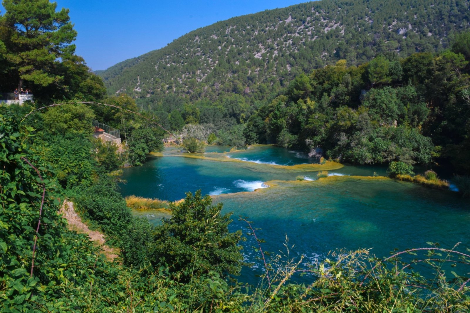 The Krka spilling through shallow cascades into turquoise pools, between wooded slopes