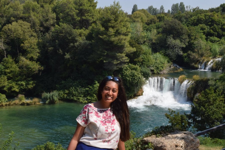 Meenu smiling above a turquoise pool, with a broad waterfall behind her
