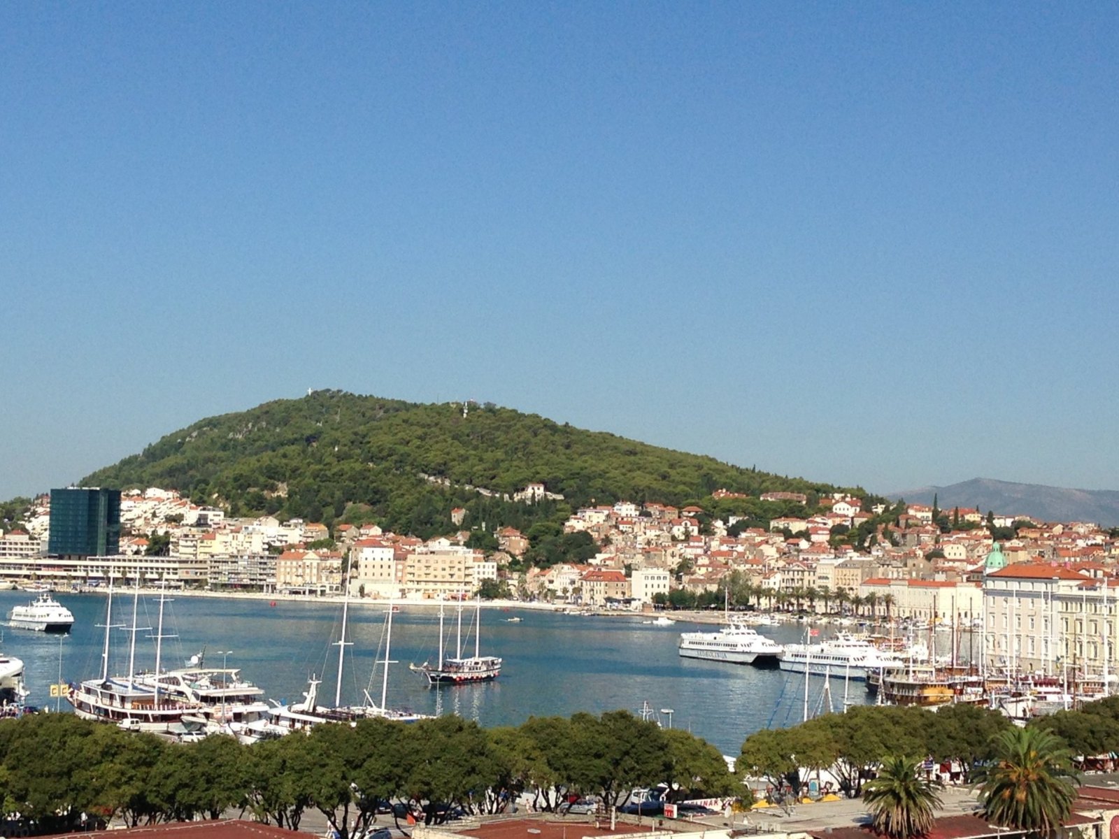 Split's harbour from above, crowded with boats, with the old town and the green hill of Marjan behind