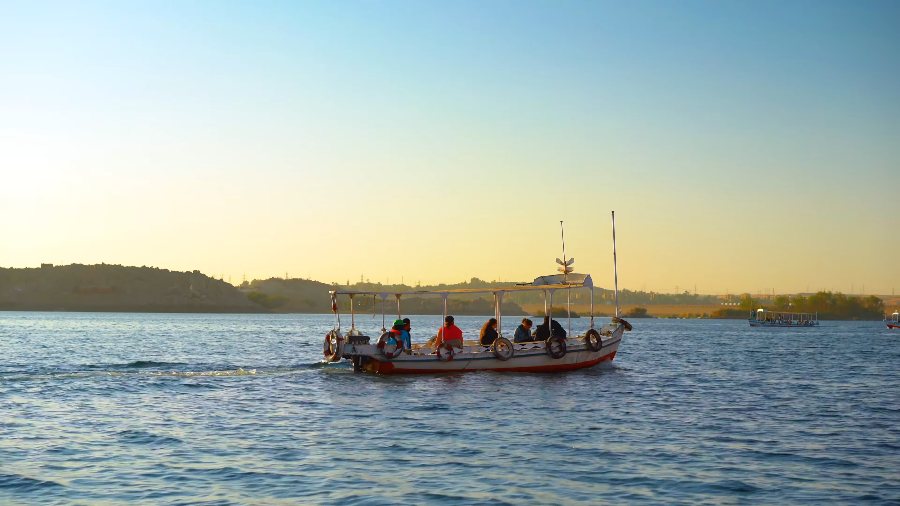 A small motorboat with passengers crossing the Nile in the late afternoon sun