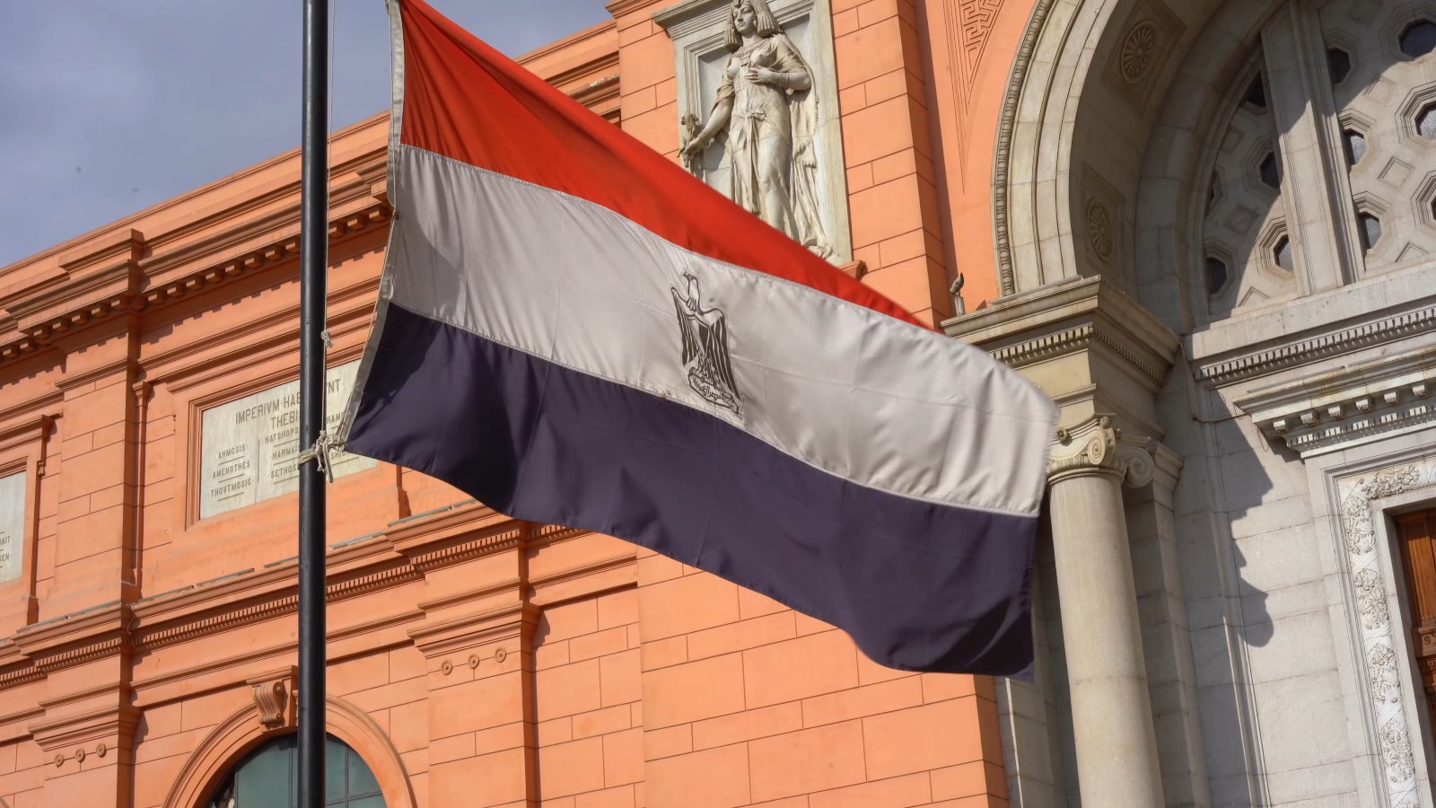Egypt's flag flying in front of the Egyptian Museum's red facade