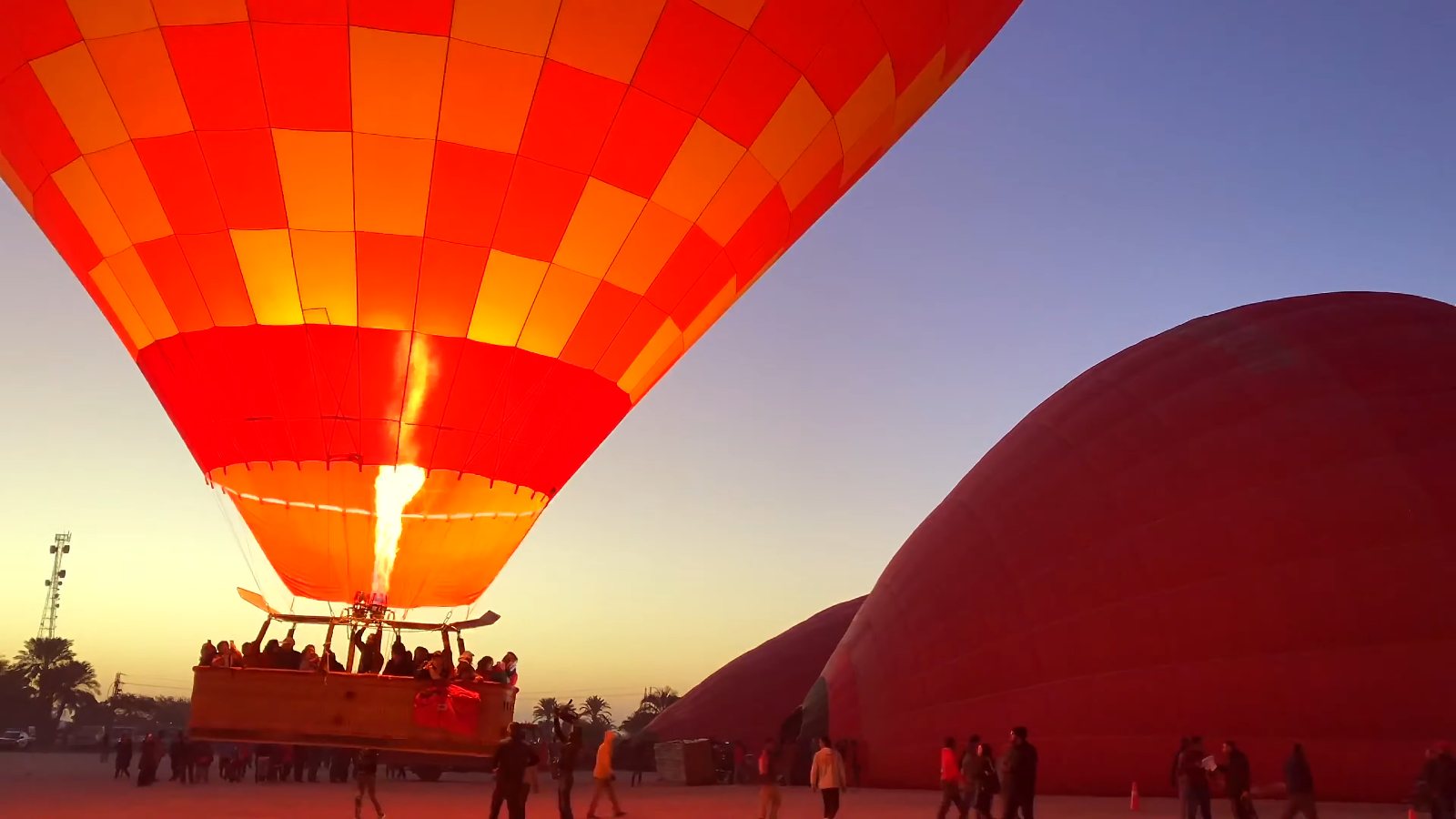 A hot air balloon lifting off at dawn with its burner lit, beside another still filling on the ground