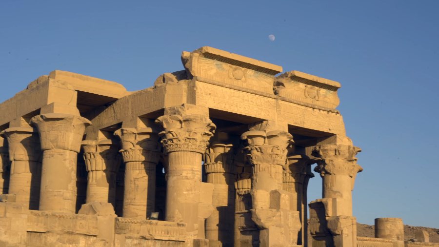 The carved columns of Kom Ombo's temple against a blue sky, with the moon above