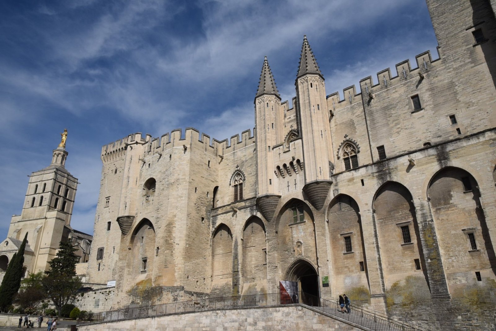 The Popes' Palace in Avignon, its pointed towers and tall arches in the sun, with the cathedral tower to the left