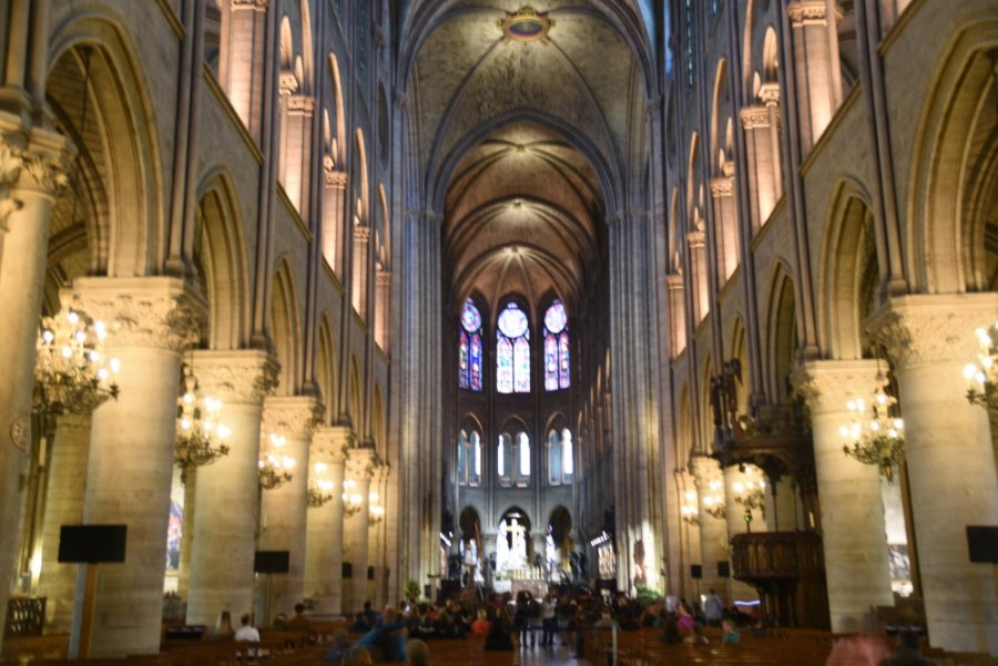Notre-Dame's long nave lit by rows of chandeliers, with tall windows glowing at the far end