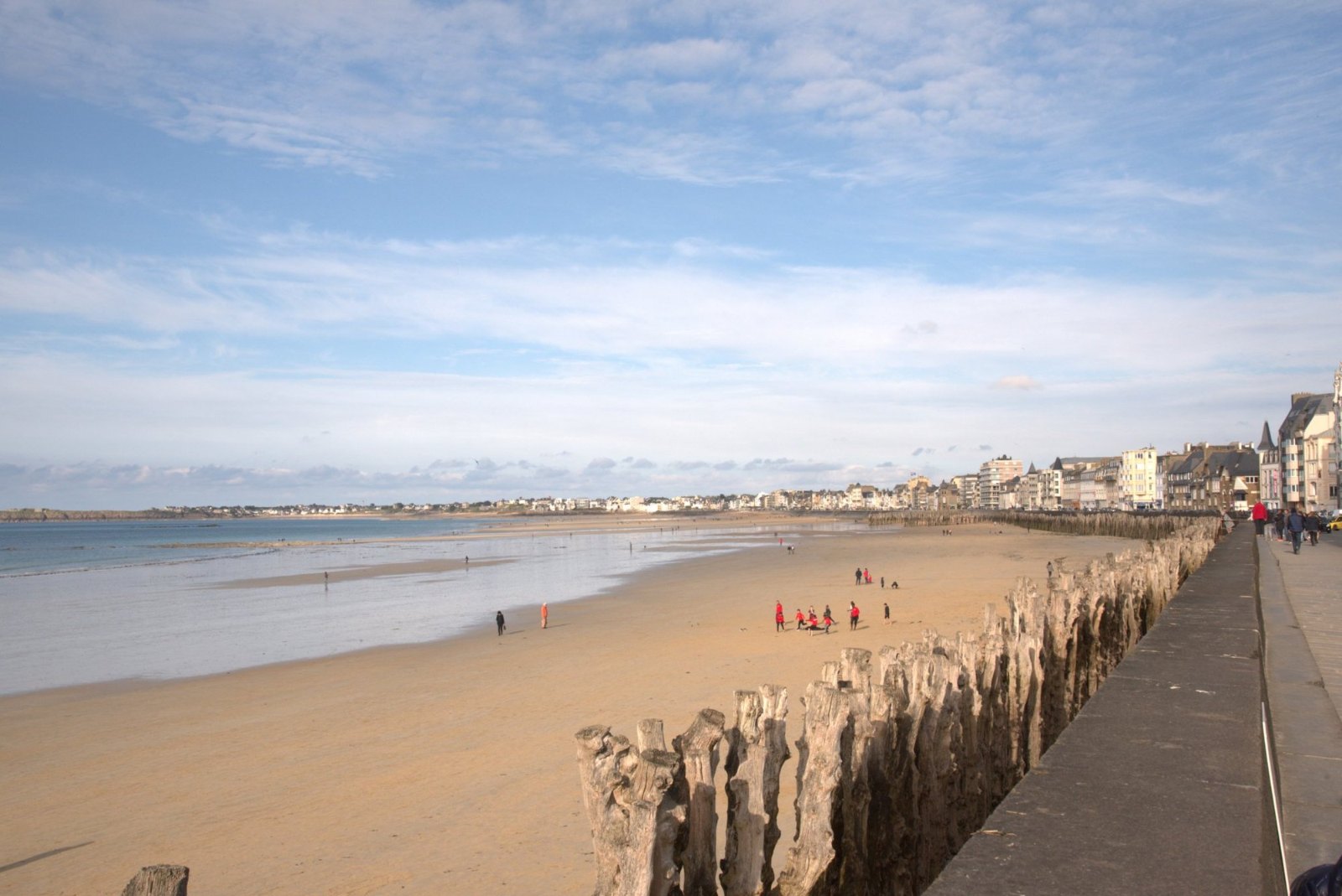 Saint-Malo's long beach at low tide, with a line of weathered wooden posts and the town along the shore