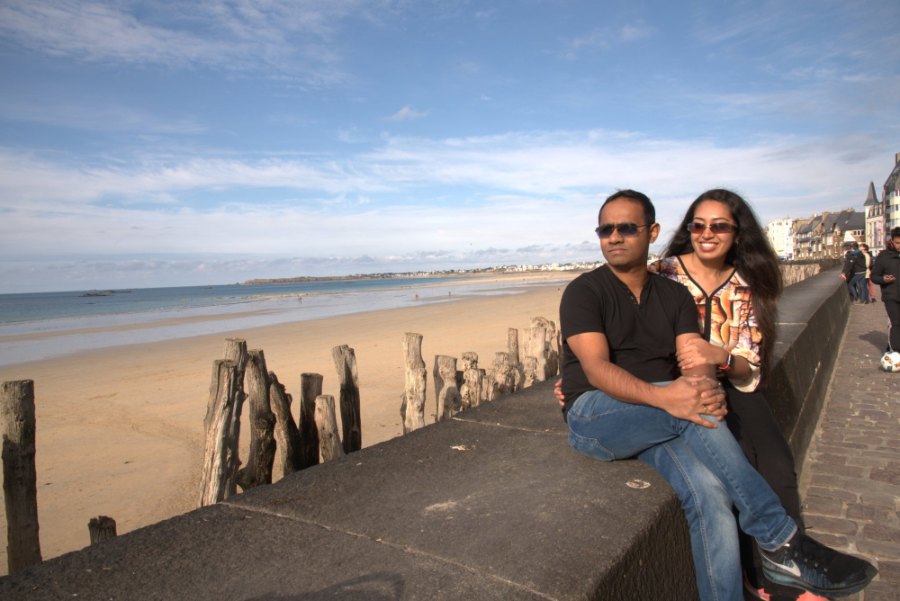 Meenu and Praddy on the sea wall above the beach, with wooden posts standing in the sand below