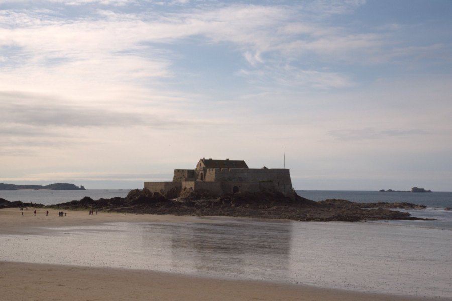 A stone fort on its rocky islet off the beach, with the tide out and the wet sand shining