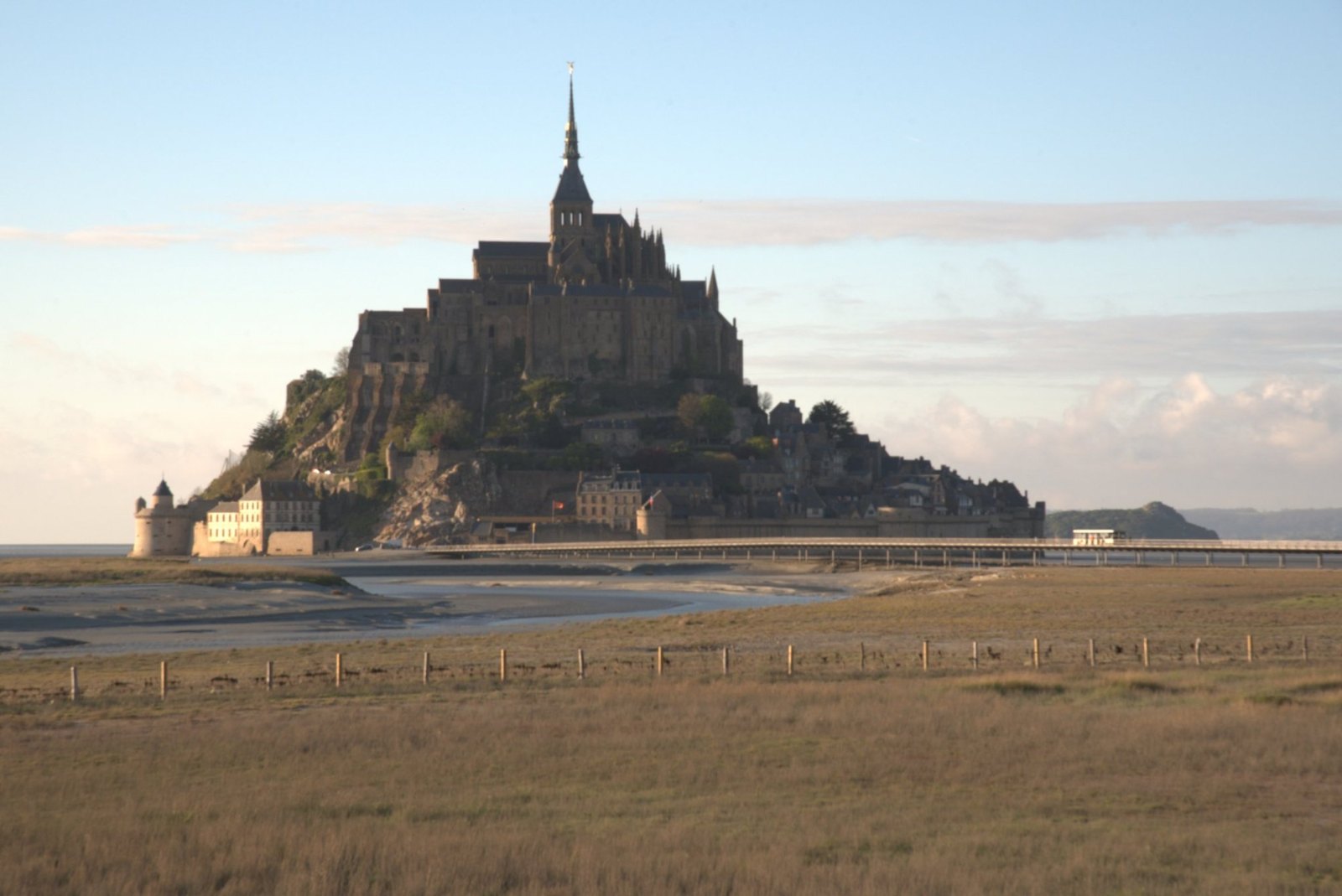 Mont-Saint-Michel in warm evening light across the meadows, with the walkway running out to its foot
