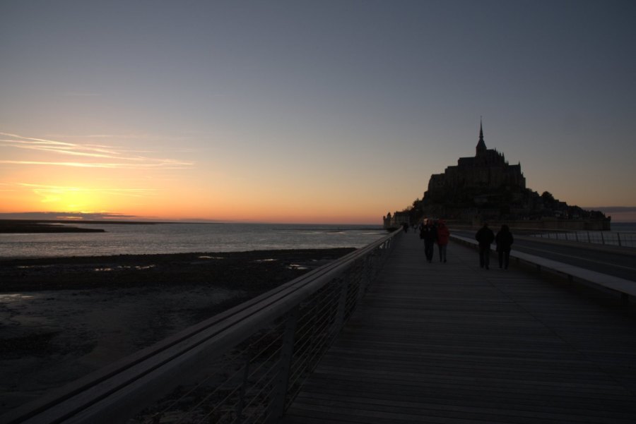 The sun going down over the bay beside the Mont, with people walking out along the walkway