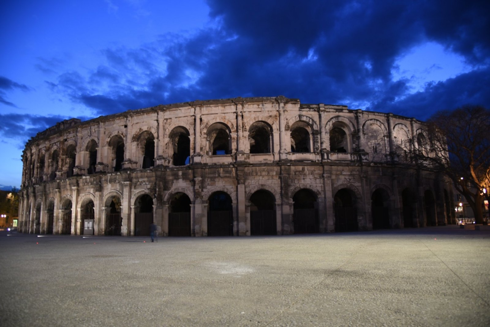 The Roman amphitheatre in Nîmes at blue hour, its two tiers of arches under a deep blue sky