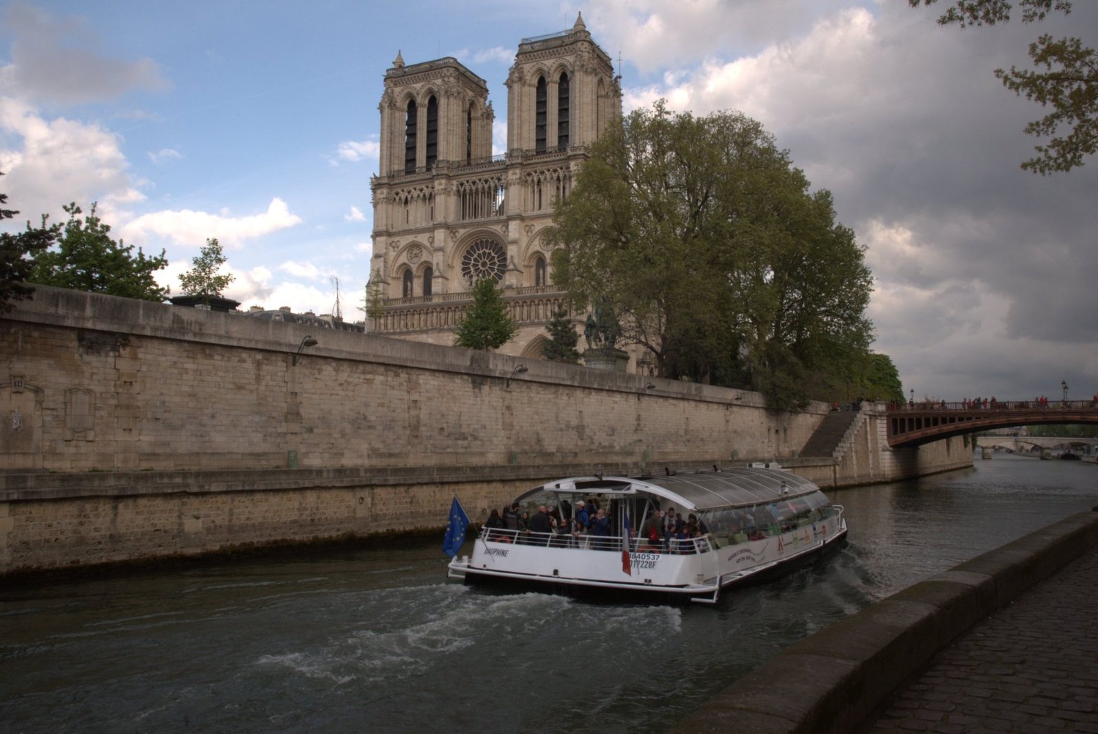 Notre-Dame's twin towers above the Seine, with a tour boat passing below the stone embankment
