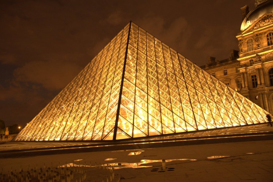 The Louvre's glass pyramid lit gold at night, beside the palace's lit façade