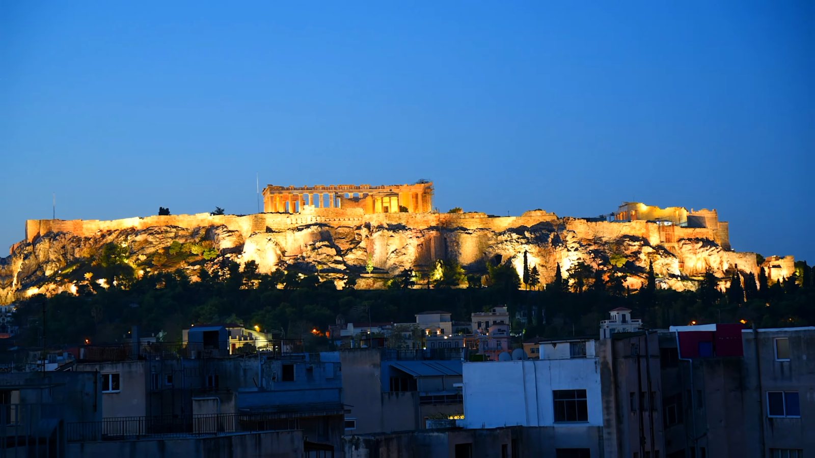 The Acropolis floodlit at dusk above the rooftops of central Athens