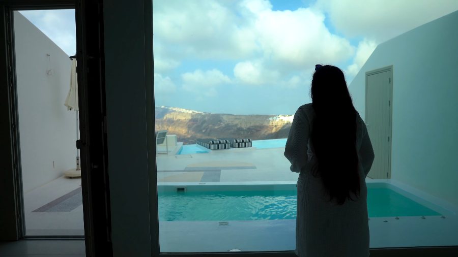 Meenu in a robe at the window, looking out over the plunge pool to the caldera