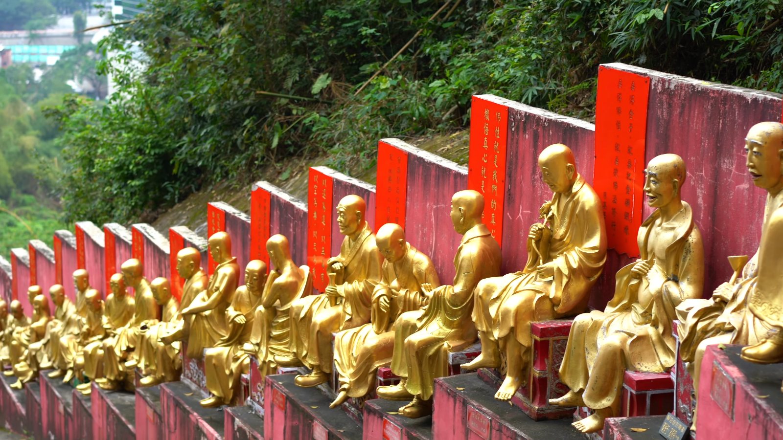 A long row of golden statues seated beside the path, each in front of a red plaque
