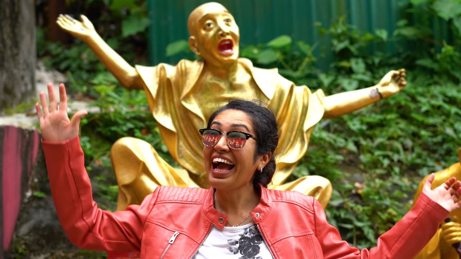 Meenu laughing with her arm thrown up, copying the golden statue behind her