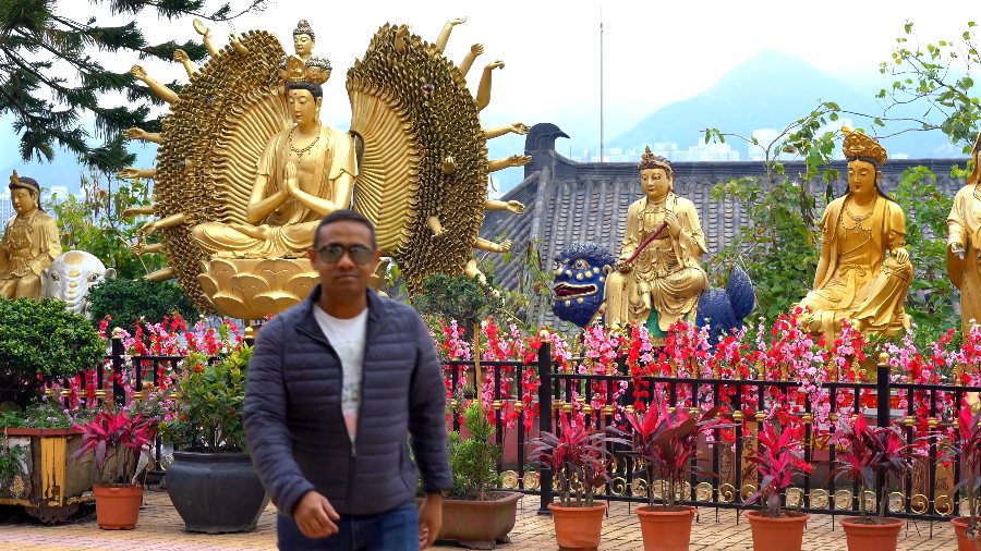 Praddy walking past pink and red flowers below a many-armed golden statue